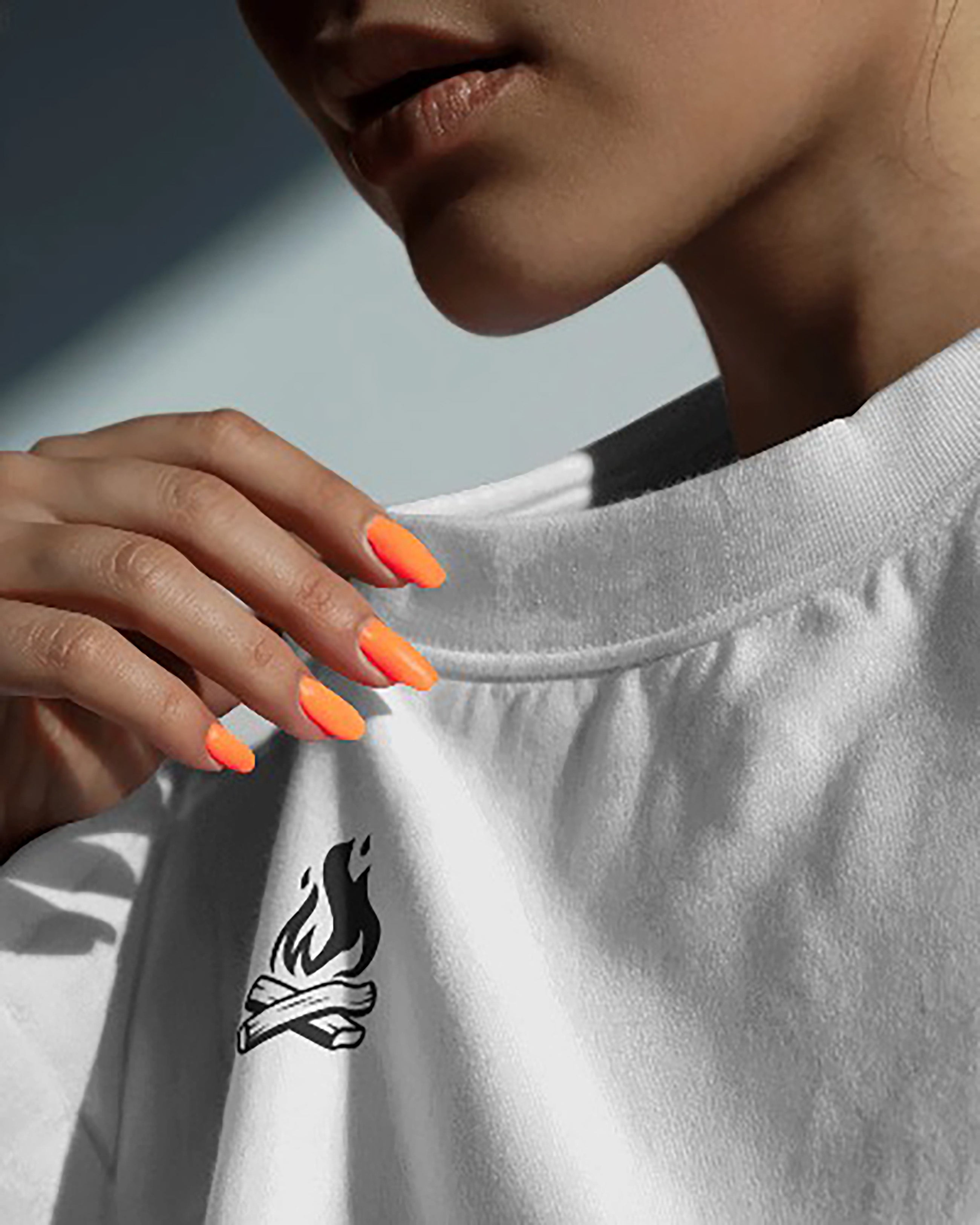 Person wearing a white t-shirt with a black campfire graphic, holding the neckline.