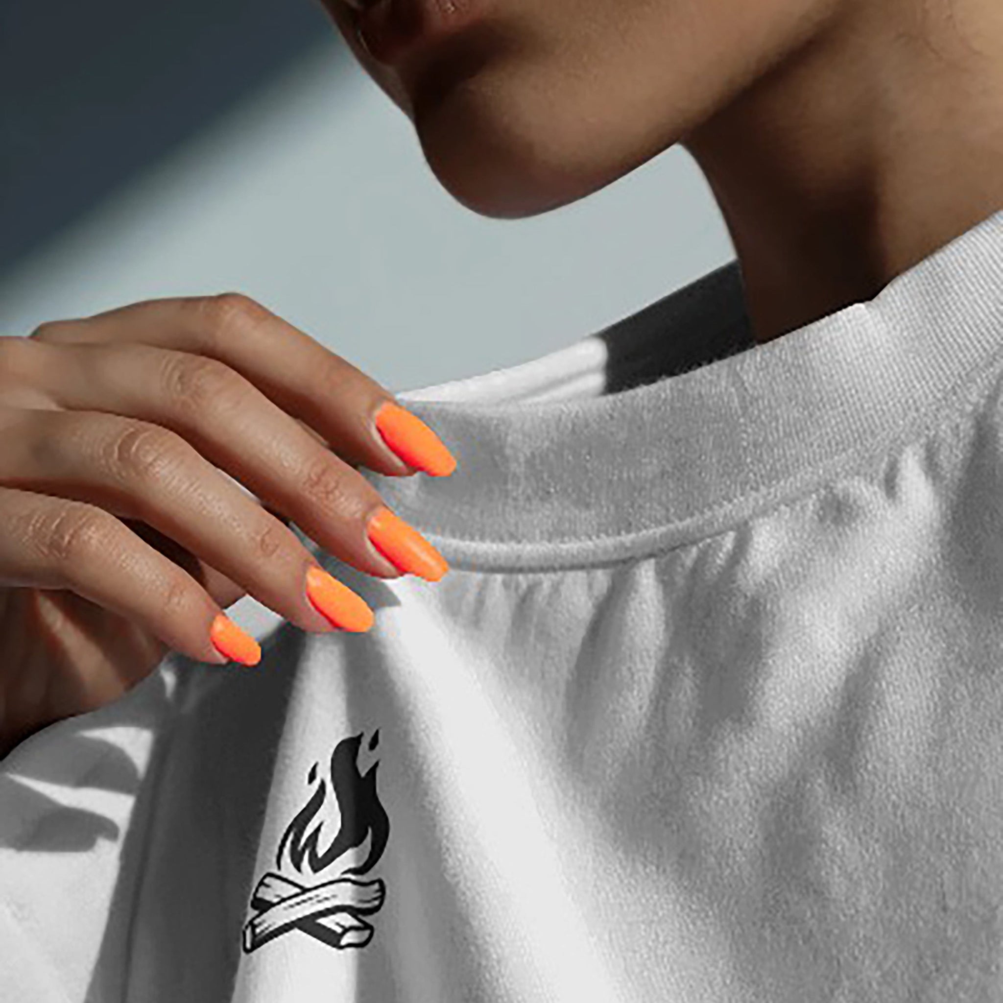 Person wearing a white t-shirt with a black campfire graphic, holding the neckline.