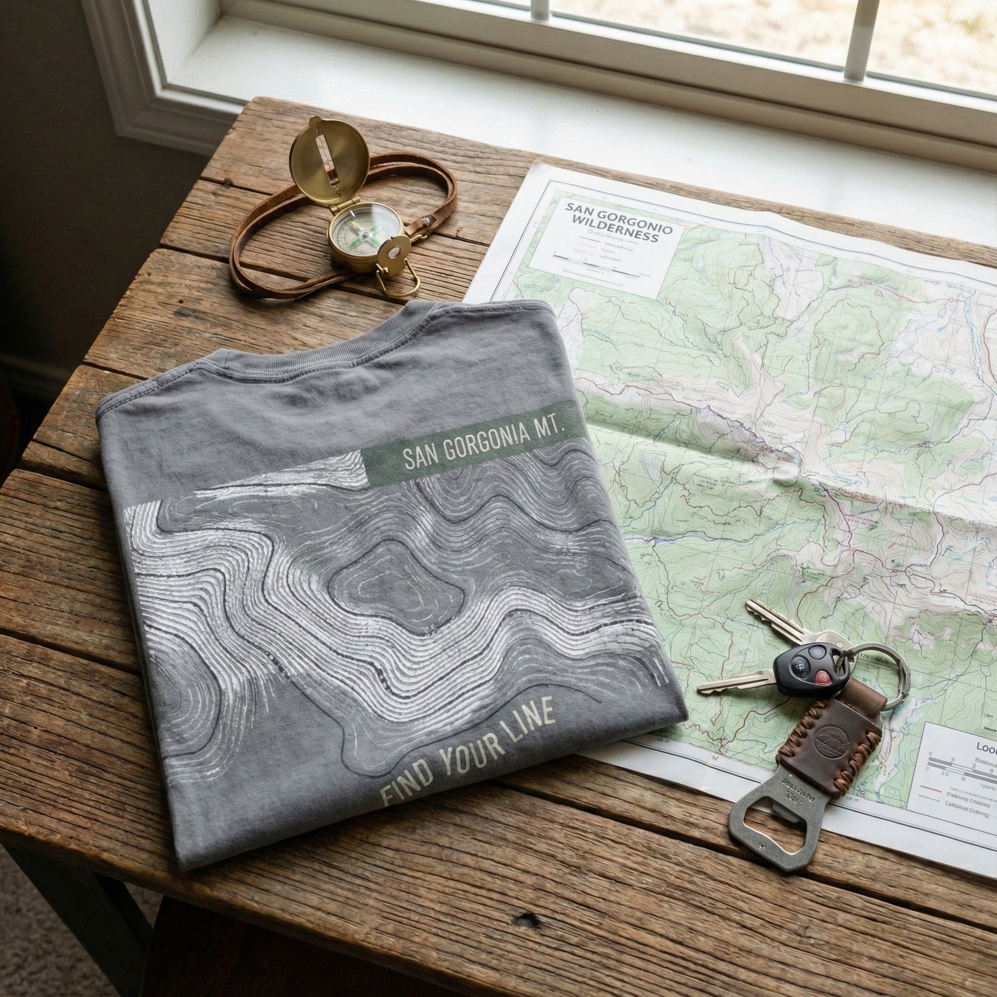 Gray t-shirt with topographic design on a wooden table with map and keys