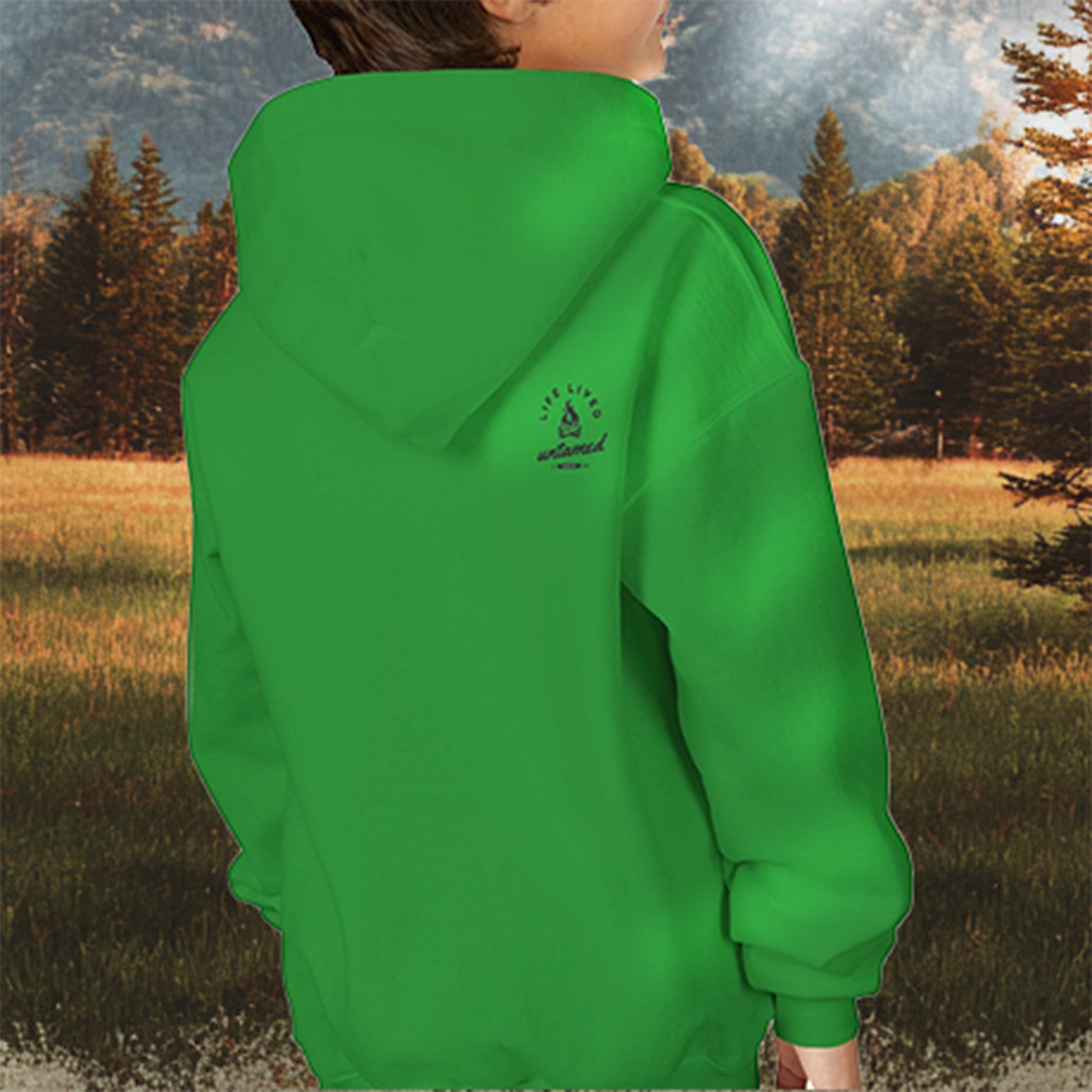 A kid wearing a green hoodie with a logo reads 'Life Lived Untamed' on the back, standing in a natural setting with trees and grass.