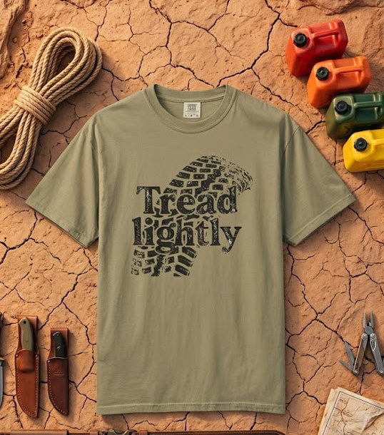 Khaki green t-shirt with 'Tread Lightly' design on a textured brown background with outdoor gear.