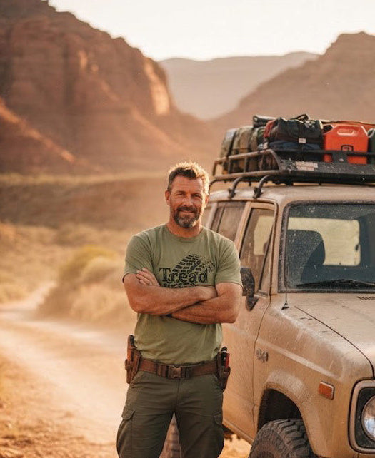 Man standing in front of a beige SUV with roof gear in a desert landscape