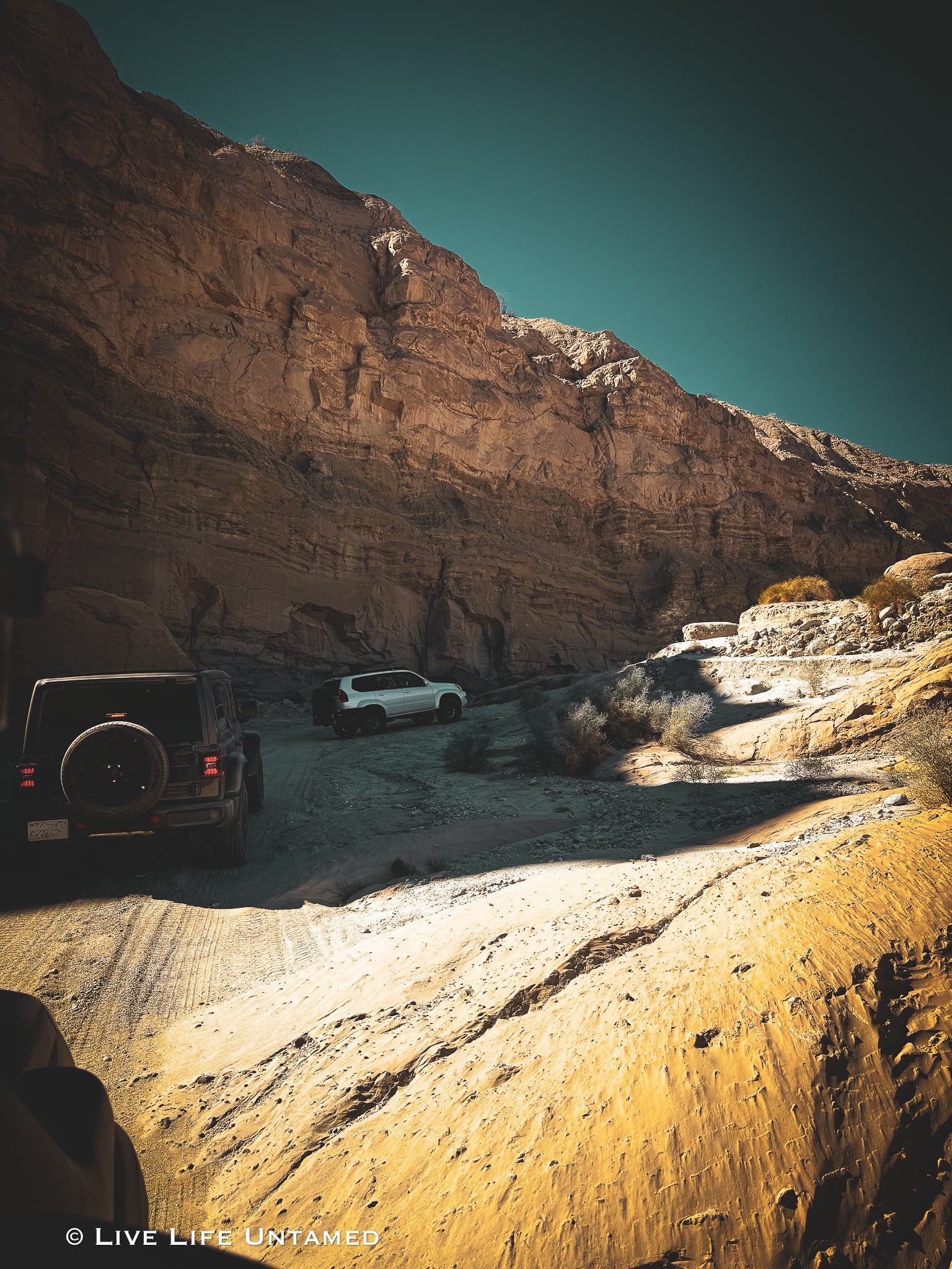 Two off-road vehicles on a rocky desert trail with mountains in the background.