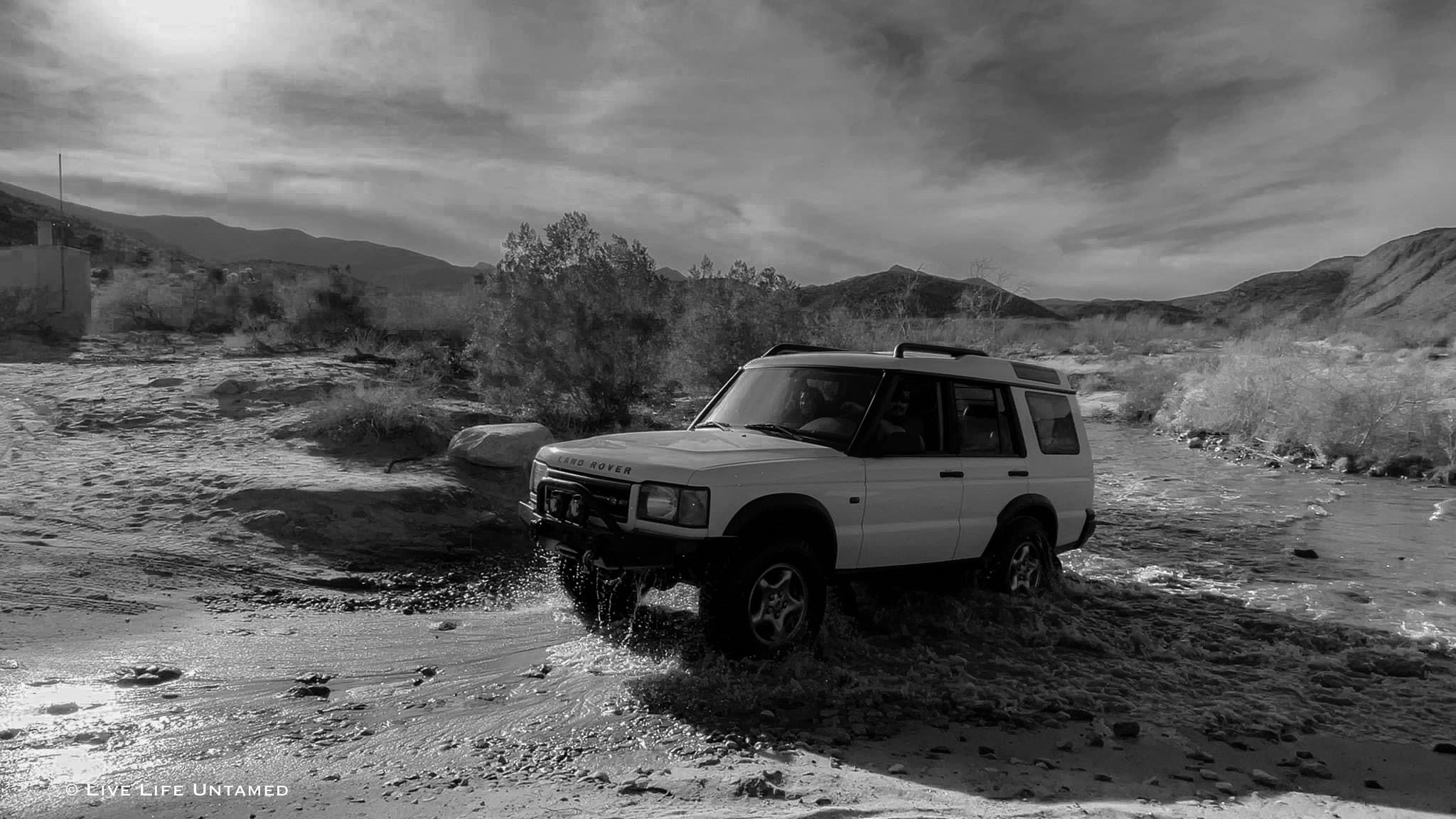 White SUV driving through a muddy desert landscape with mountains in the background.