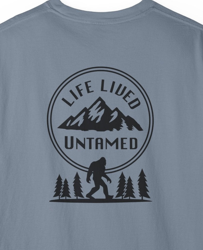 A close up of blue Jean t-shirt with a graphic design on the back featuring mountains, trees, and a silhouette of a Sasquatch.
