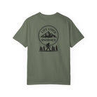 Sage Green t-shirt with a black graphic design on the back featuring mountains, trees, and a silhouette of a Sasquatch
