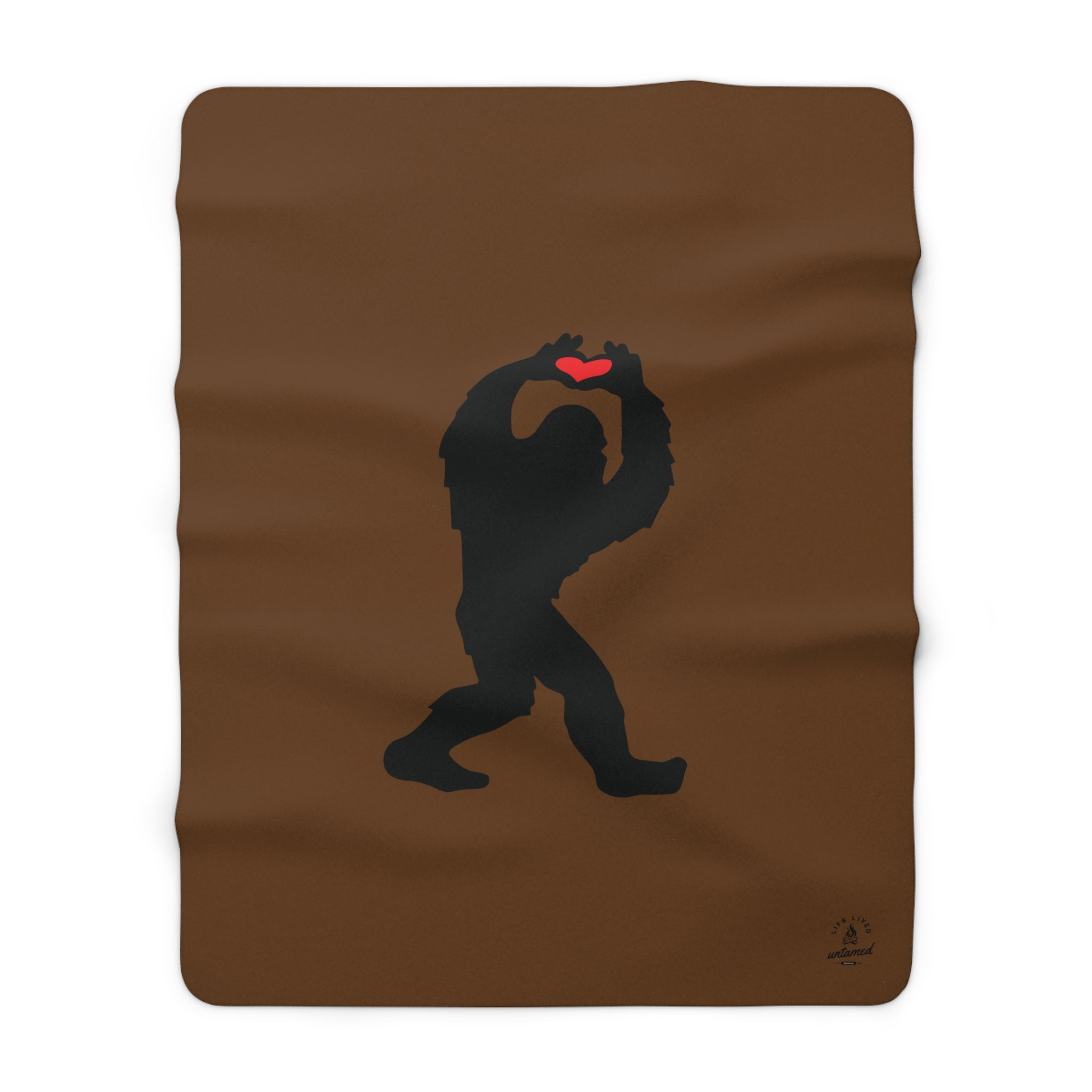 Brown sherpa blanket with a black silhouette of a Sasquatch holding a red heart on a white background