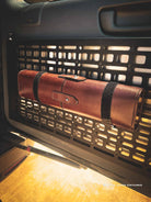 Brown leather tool-roll mounted on molle panel with black Velcro straps inside a vehicle's open door