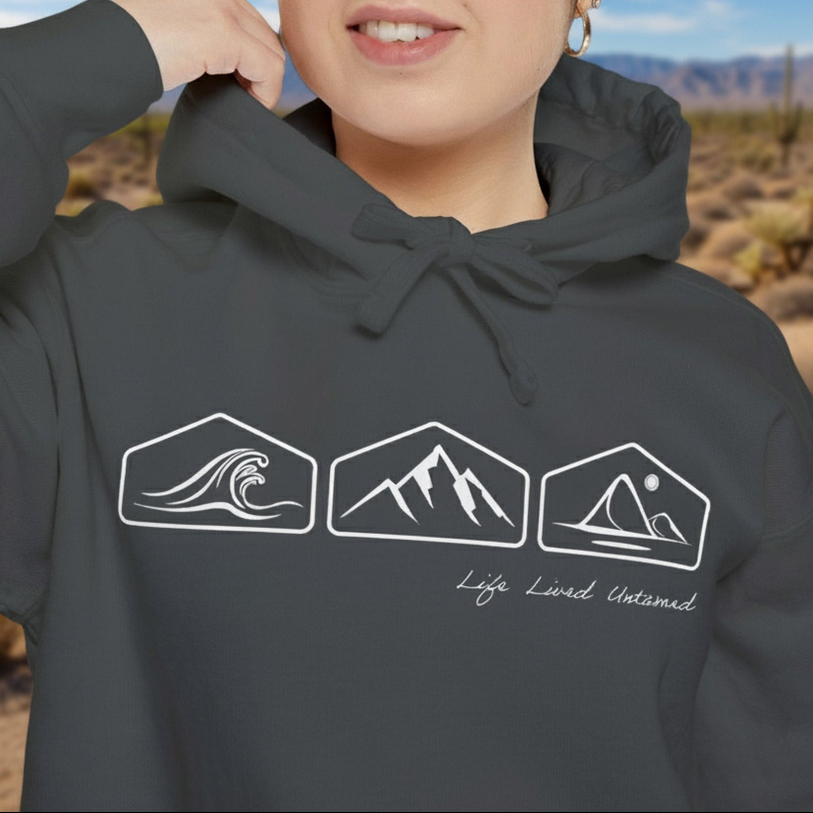 A person wearing a black hoodie with nature-themed designs and text in a desert setting