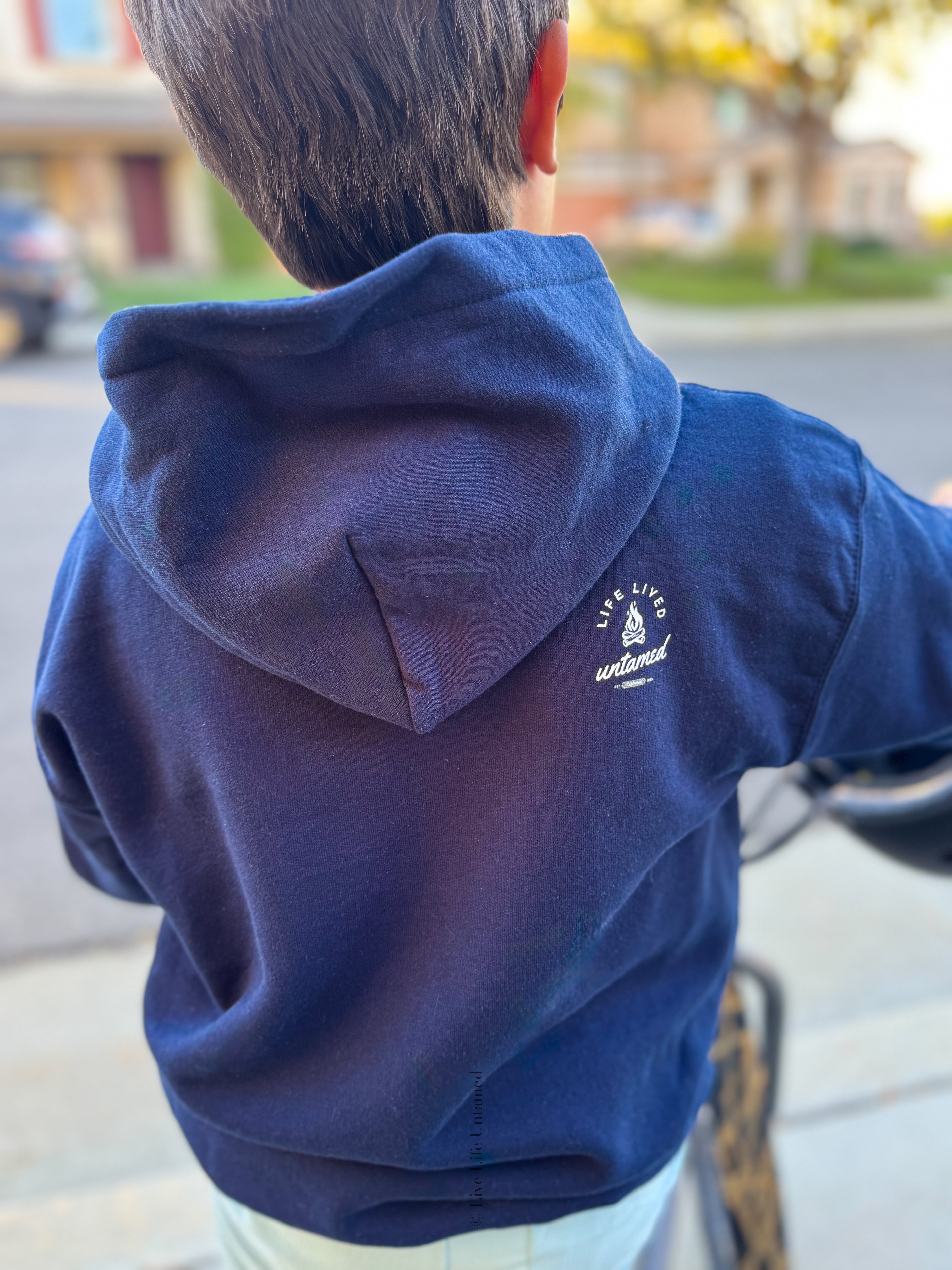 A close-up photo from behind of a young boy with a small white logo on the back of the sweatshirt that reads 'LIFE LIVED Untamed'.