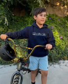 A young boy wearing a navy blue hooded sweatshirt with a horizontal row of  mountain, desert, and wave graphics on the front. 