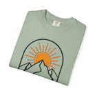 Folded bay green t-shirt with mountain and sun graphic on a white background